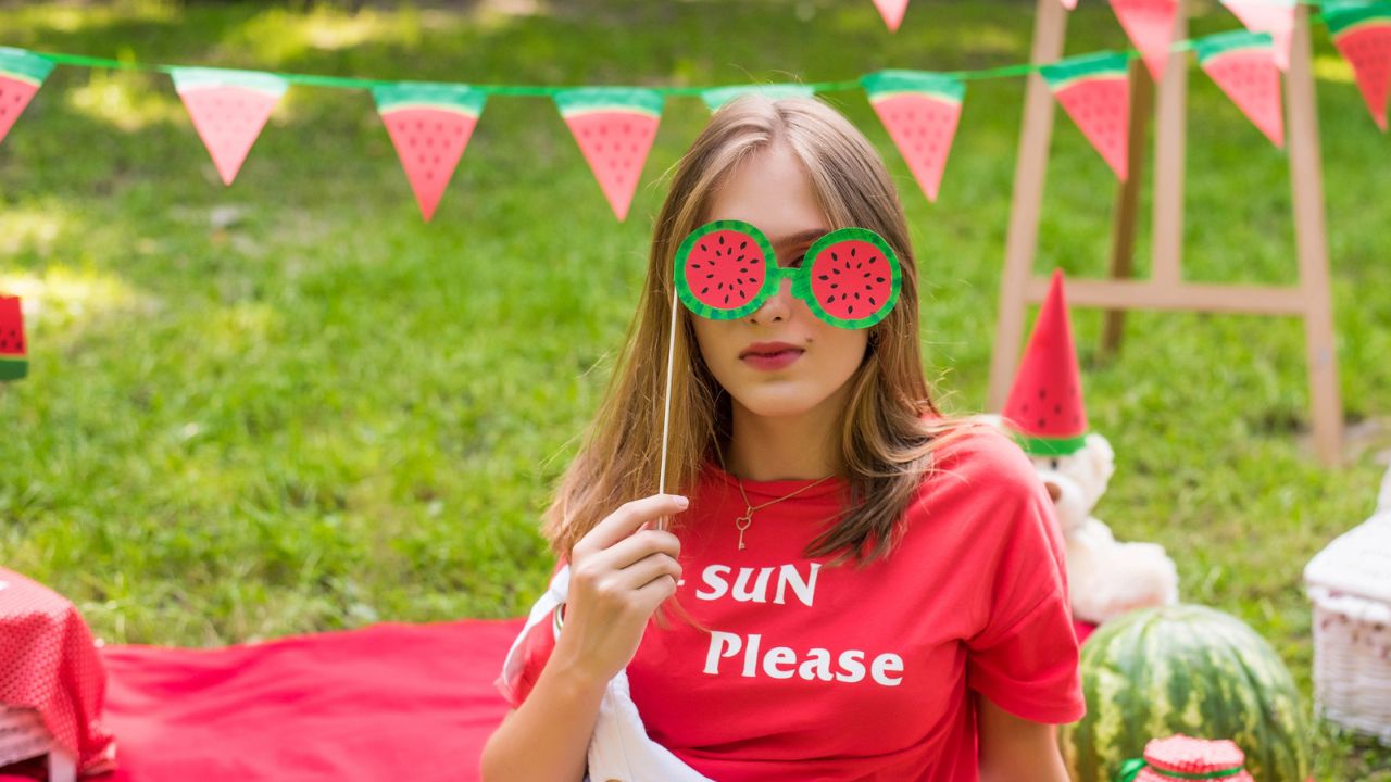 Woman holding a watermelon-shaped photo prop at an outdoor event.