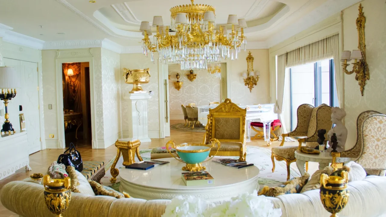 A luxury hotel suite with crystal chandelier, wall sconces, cozy sofa and armchairs, and gold decor accents.