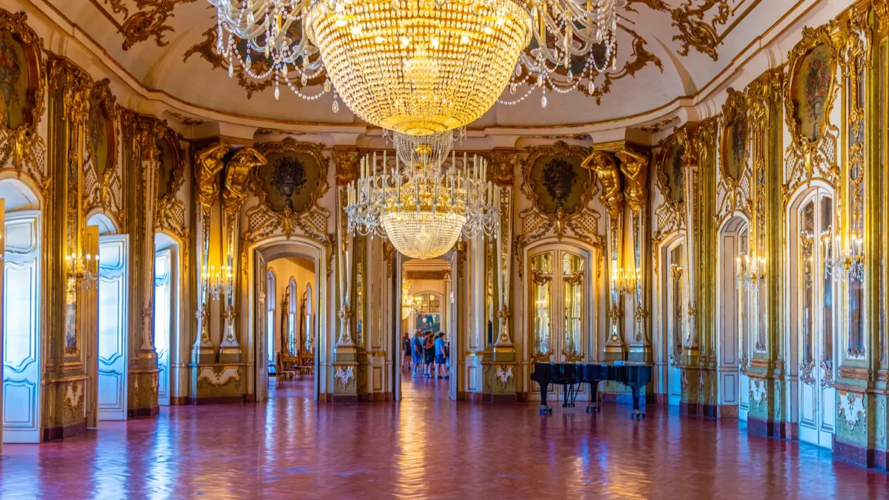 A grand ballroom interior with large crystal chandelier, ornate ceiling, and gold finishing on the walls.