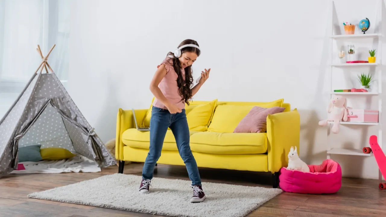preteen girl in wireless headphones holding smartphone and dancing in