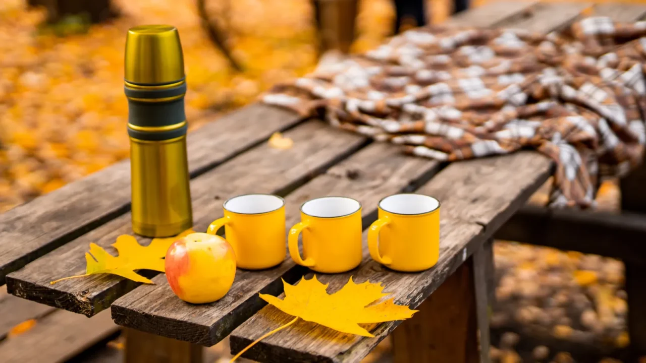 thermos with mugs and apple on the wooden table in