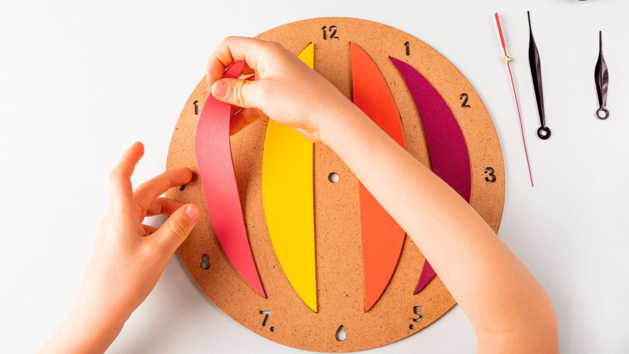 Hands assembling a colorful paper clock with orange, yellow, and purple sections.