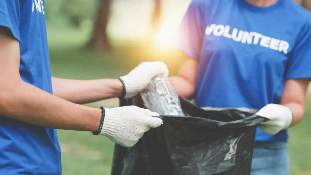 young asian volunteers with garbage bags cleaning park area ecology
