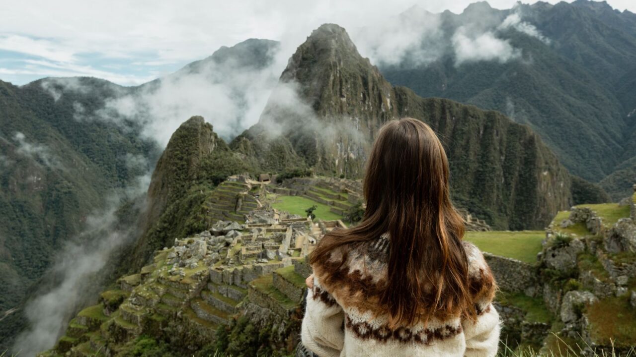 A woman in an Alpaca sweater admires the view of Machu Picchu ruins, Peru.
