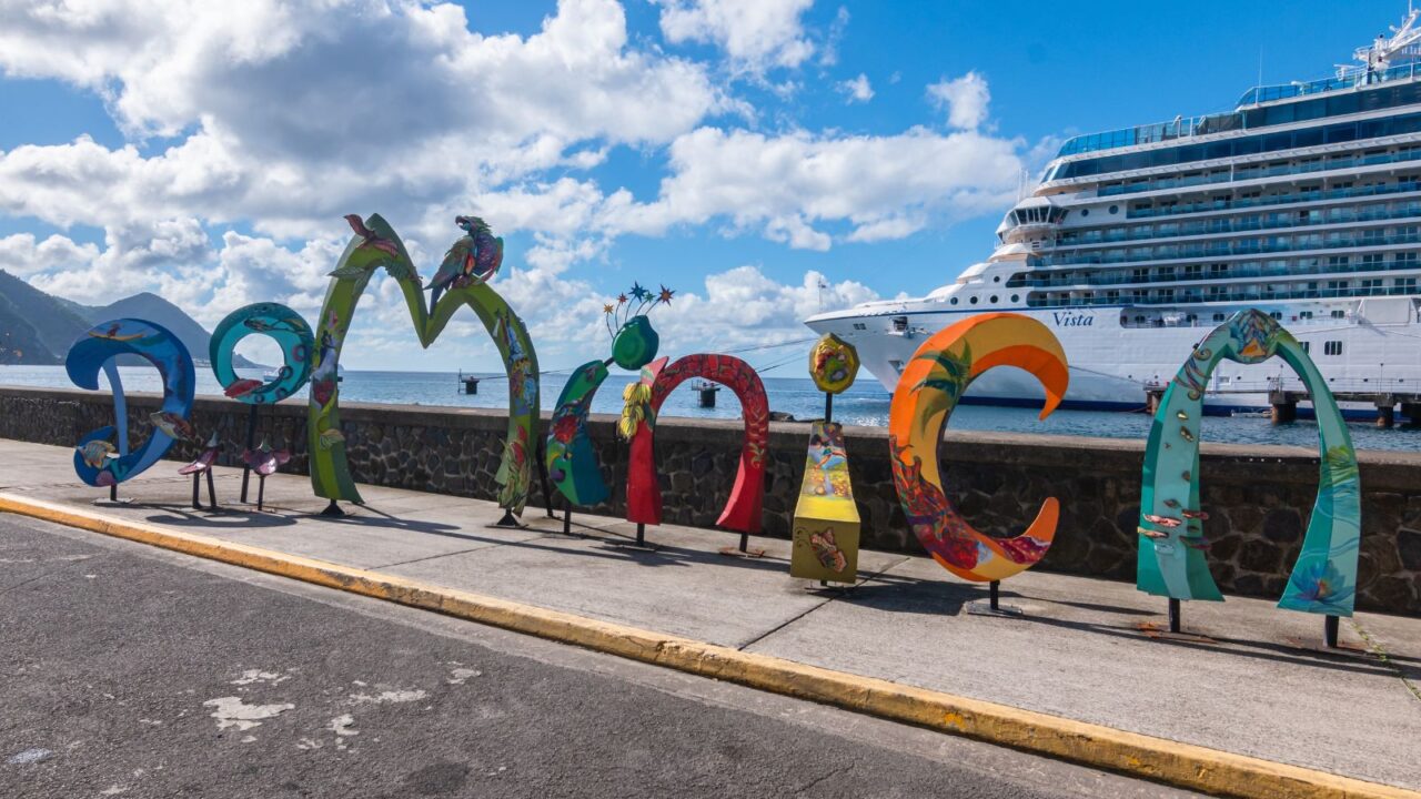 Dominica word sign in front of Oceania Cruises Vista ship in cruise port of Roseau.