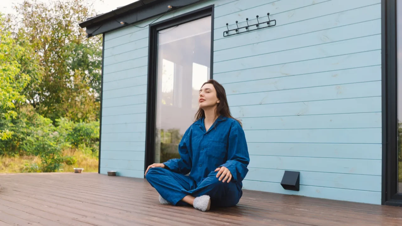A woman is sitting cross-legged on a wooden deck, practicing meditation.