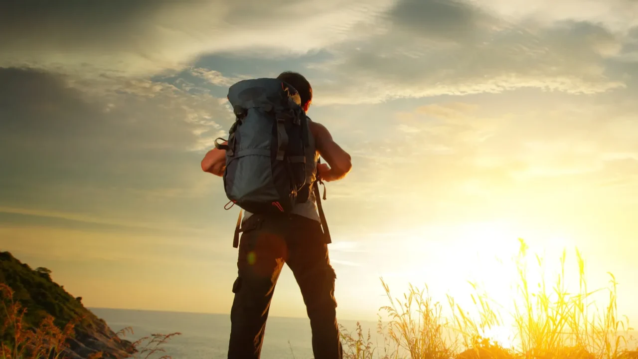 Hiker standing on a cliffside trail at sunrise.