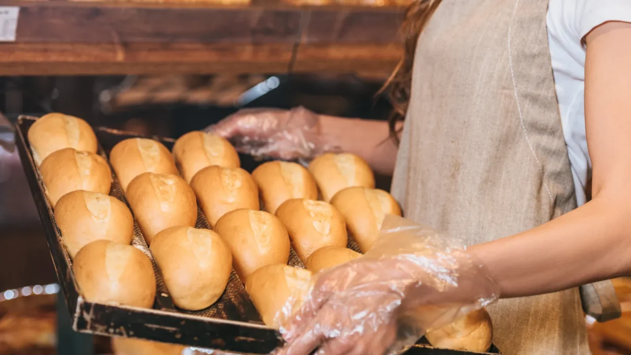 partial view of shop assistant arranging loafs of bread in