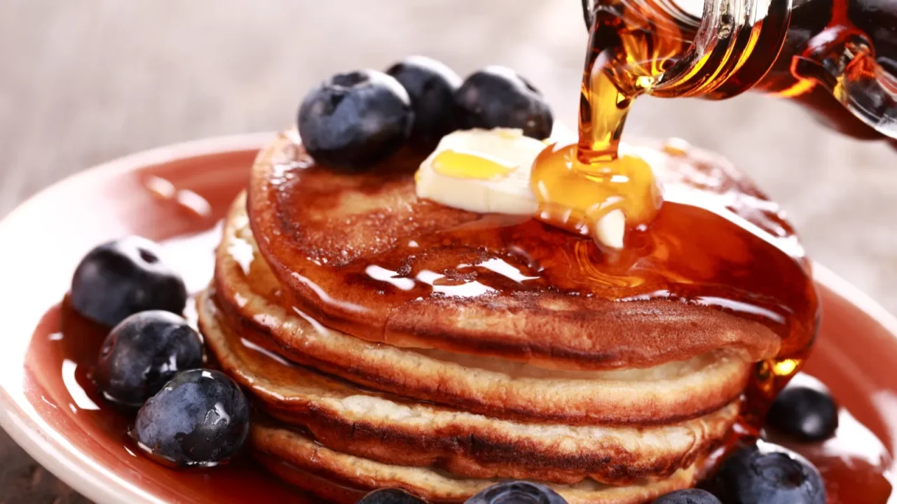 pouring maple syrup on stack of pancakes