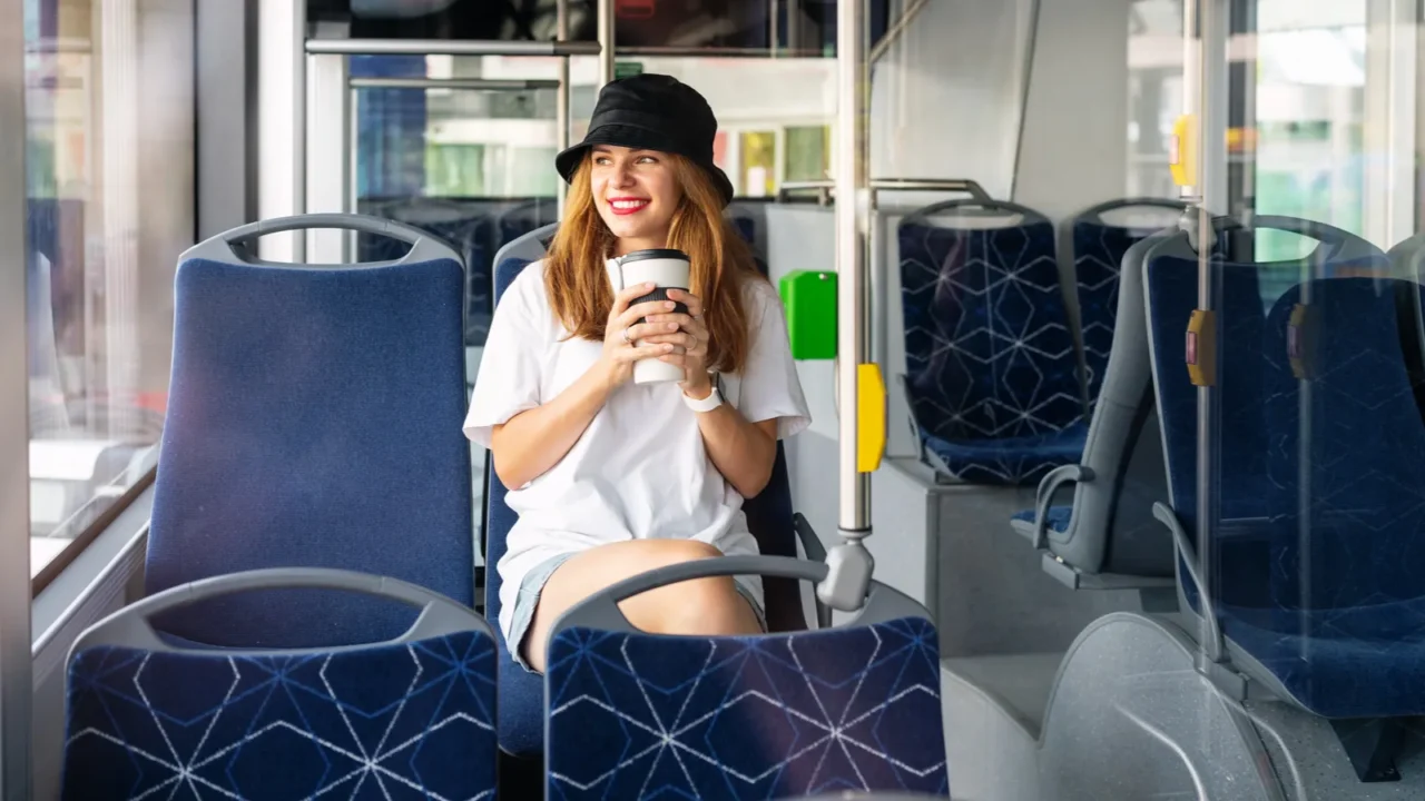 young woman with travel coffee mug travels by city bus