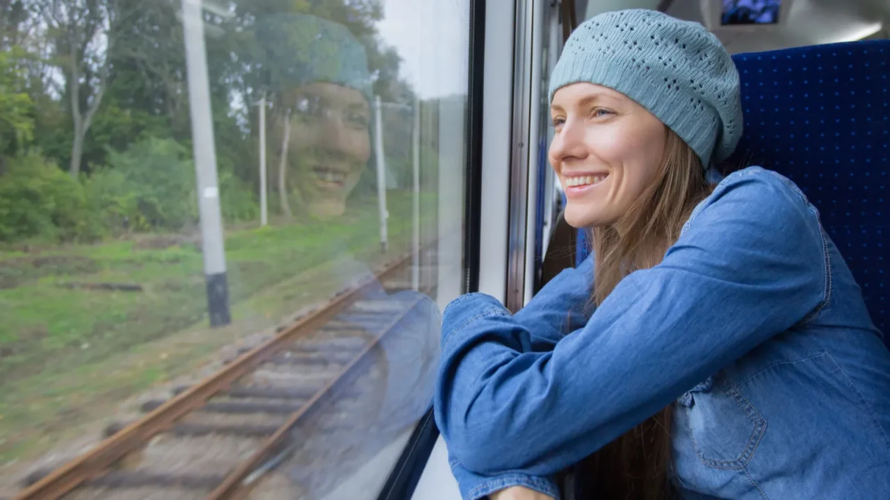 Beautiful girl traveling by train and using phone looking out of window.
