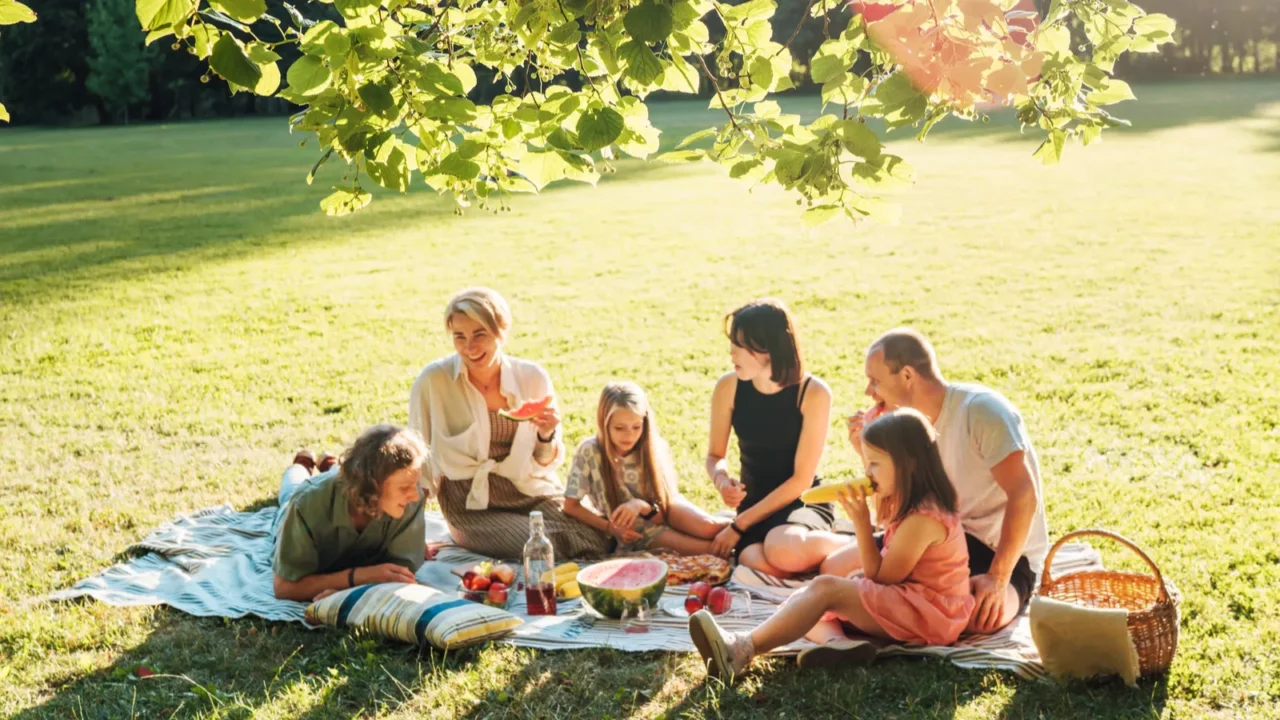big family under linden tree on the picnic blanket on