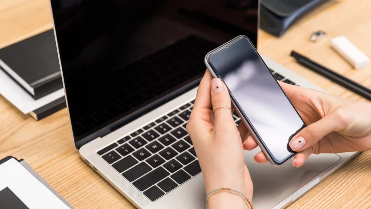 cropped shot of businesswoman using smartphone at workplace with laptop