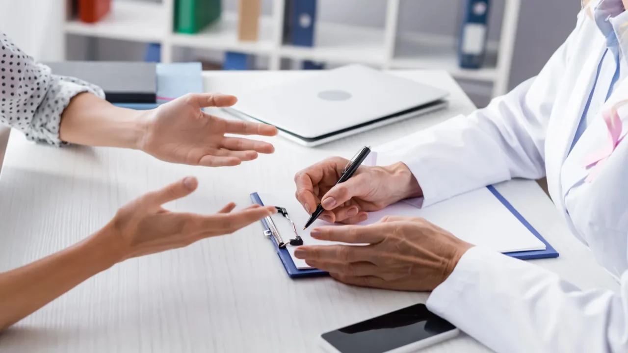 cropped view of patient and doctor writing on clipboard at