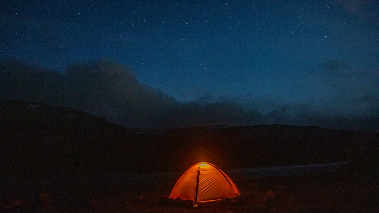 glowing orange tent in the mountains under dramatic evening sky