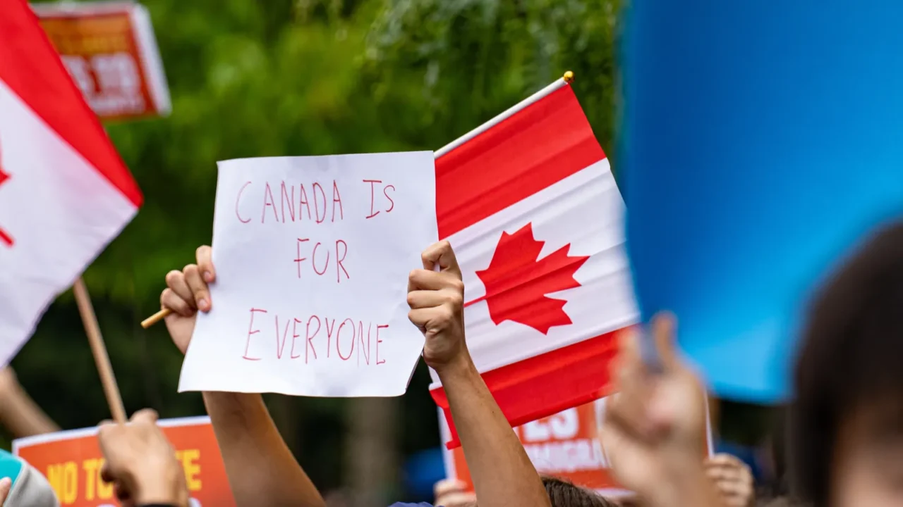View of protester holding Canada flag and sign saying Canada is for everyone at pro-immigrant rally. Toronto, Canada.