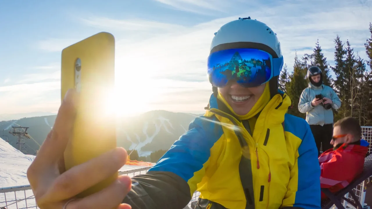 woman in ski equipment taking selfie on sunset in snowed