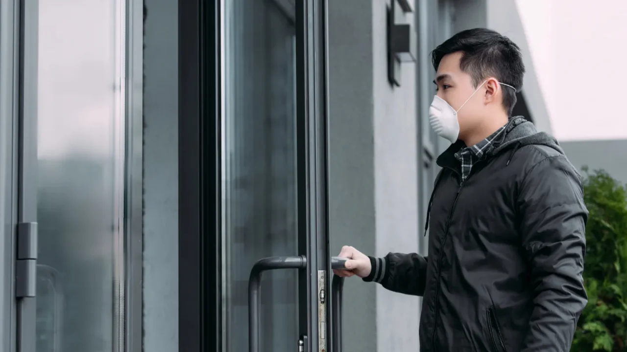 young asian man in respirator mask opening door and entering