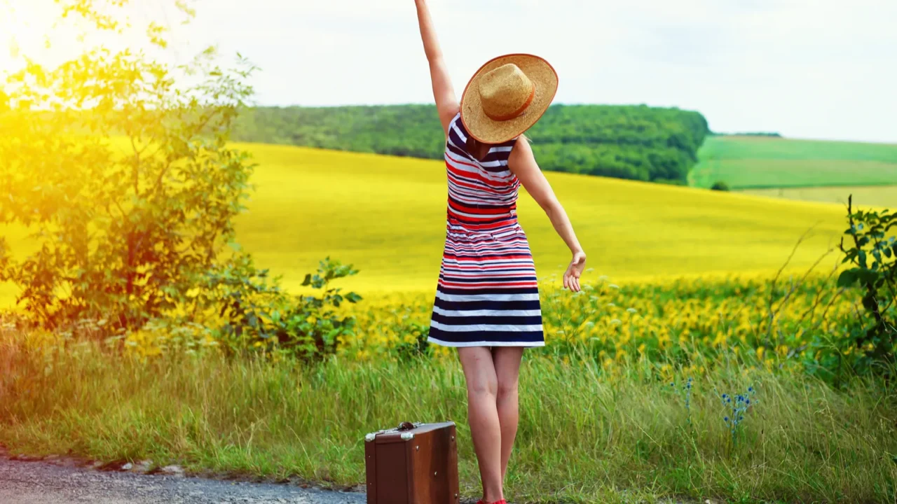 girl with old suitcase standing on roadside in sun flare