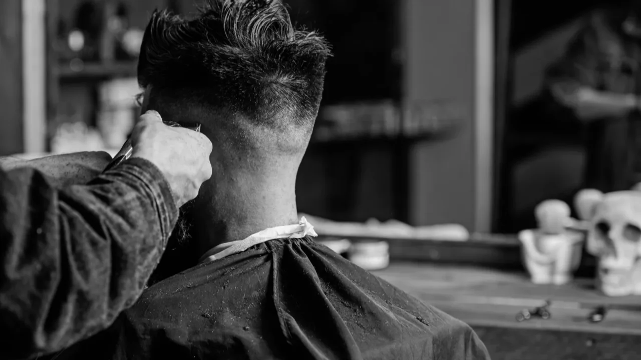 hands of barber trimming hair of bearded guy with clipper