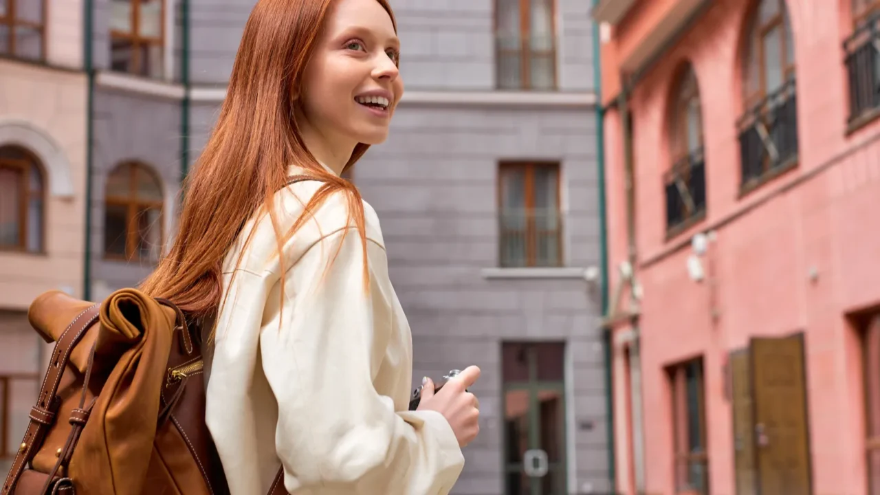 happy redhead female tourist in coat standing on street of