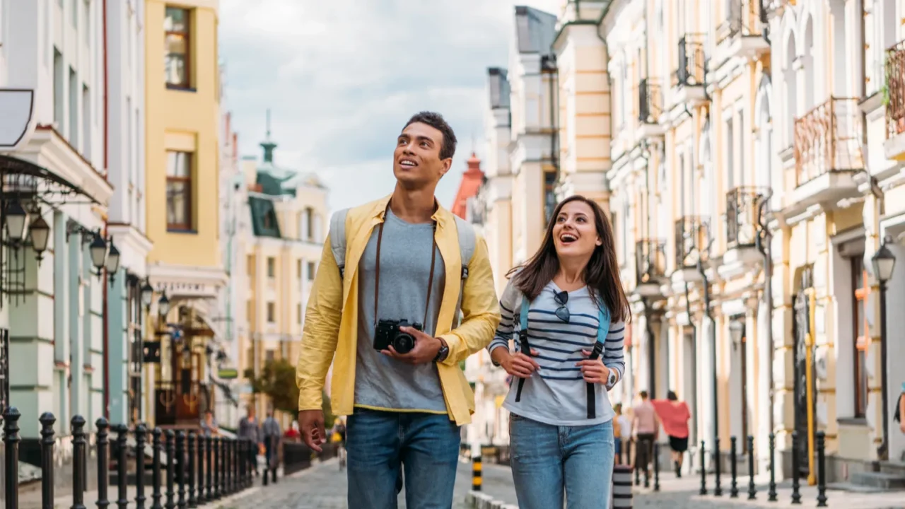 happy traveler walking with handsome biracial man near buildings