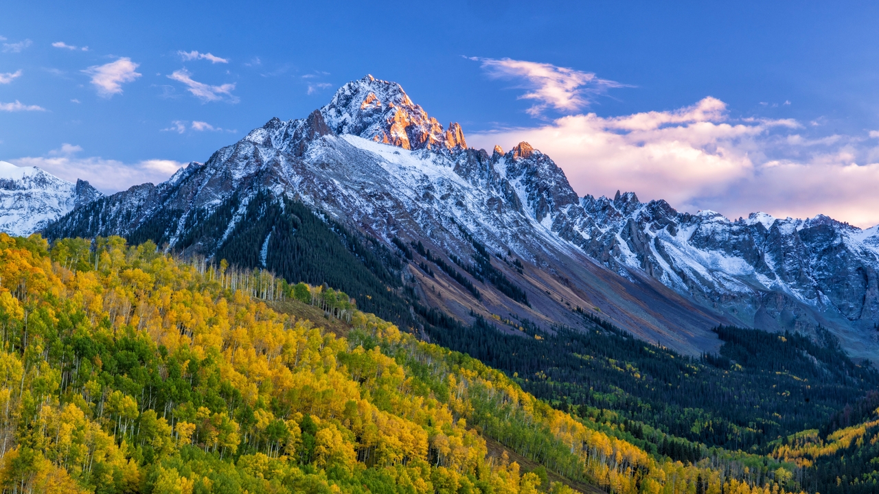 The last light of the setting sun hits the crags atop Mount Sneffels, with a mostly golden grove of quaking aspens below, in the San Juan Mountains near Ridgway, Colorado.,