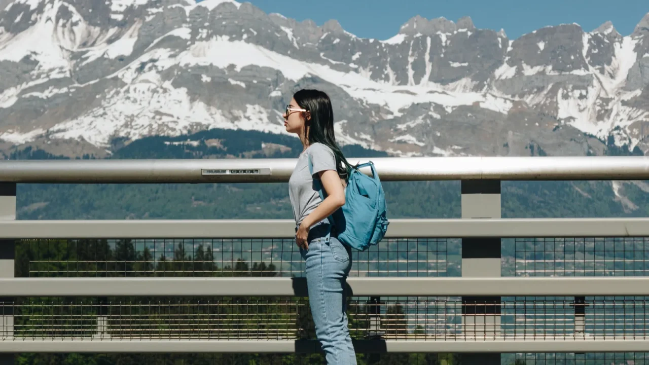 side view of girl with backpack standing near fence in