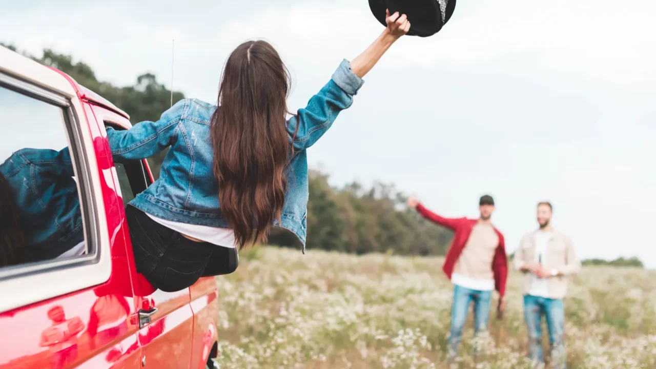 young woman outstretching from car window and greeting to men