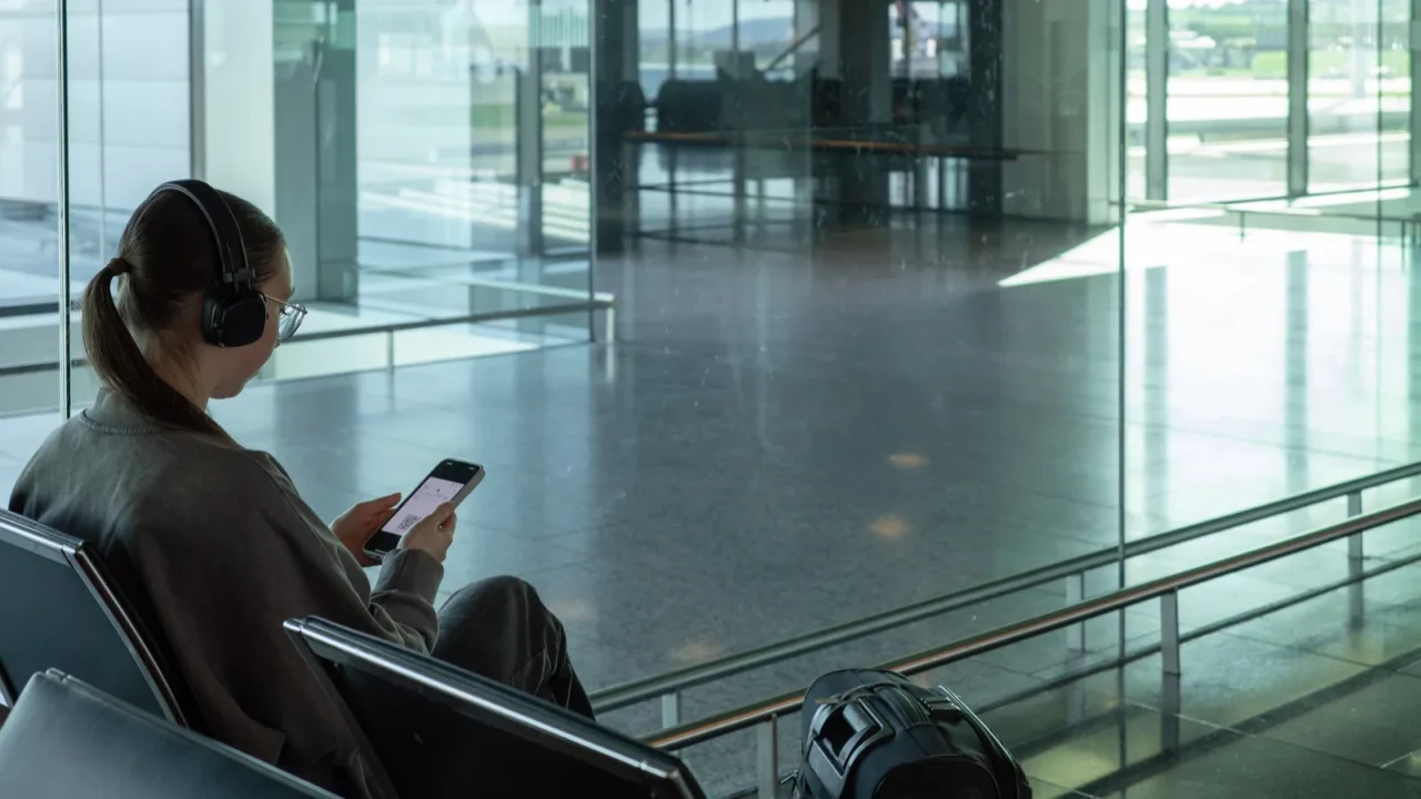young woman sitting at airport gate using smartphone and looking