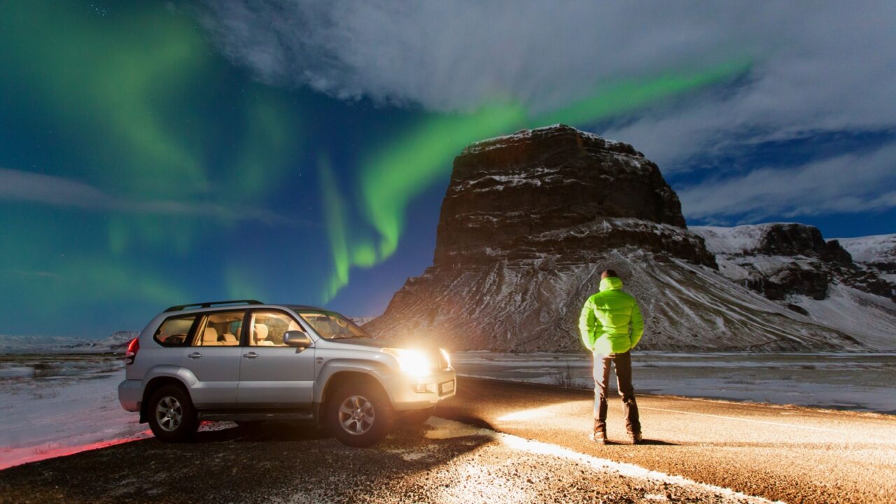 Aurora borealis above the man and car. Jokulsarlon glacier lagoon, Iceland. Green northern lights. Starry sky with polar lights. Night winter landscape with aurora. Astronomy background