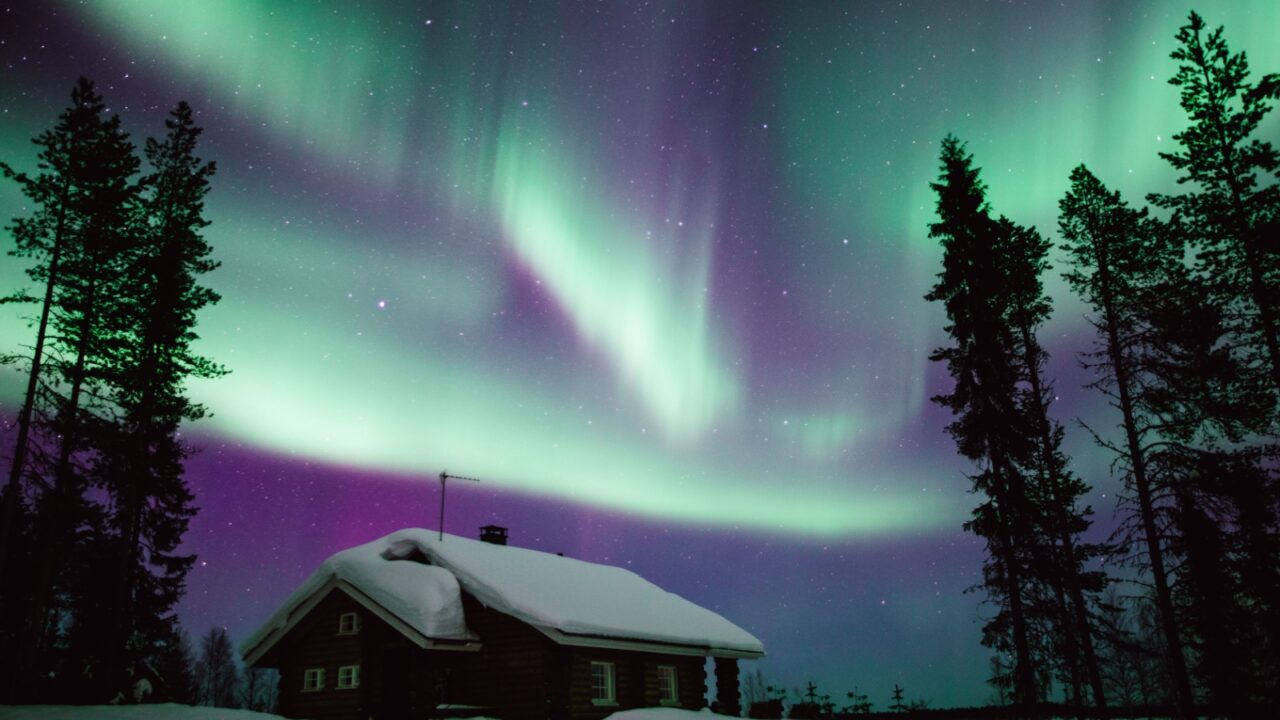 Northern lights Aurora Borealis activity over wooden cottage in winter Finland, Lapland