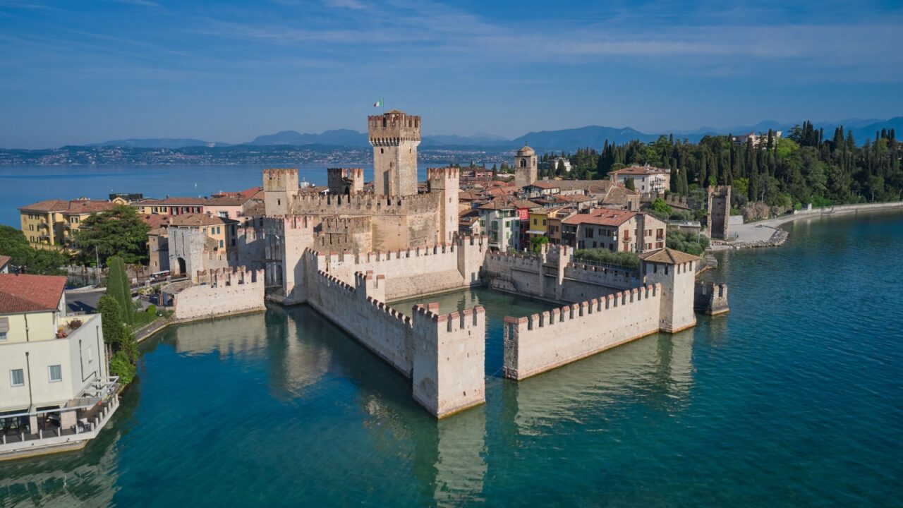 Scaligero Castle drone view. Italian castles Scaligero on the water. Flag of Italy on the towers of the castle on Lake Garda. Popular travel destination on Lake Garda in Italy. Sirmione top view.