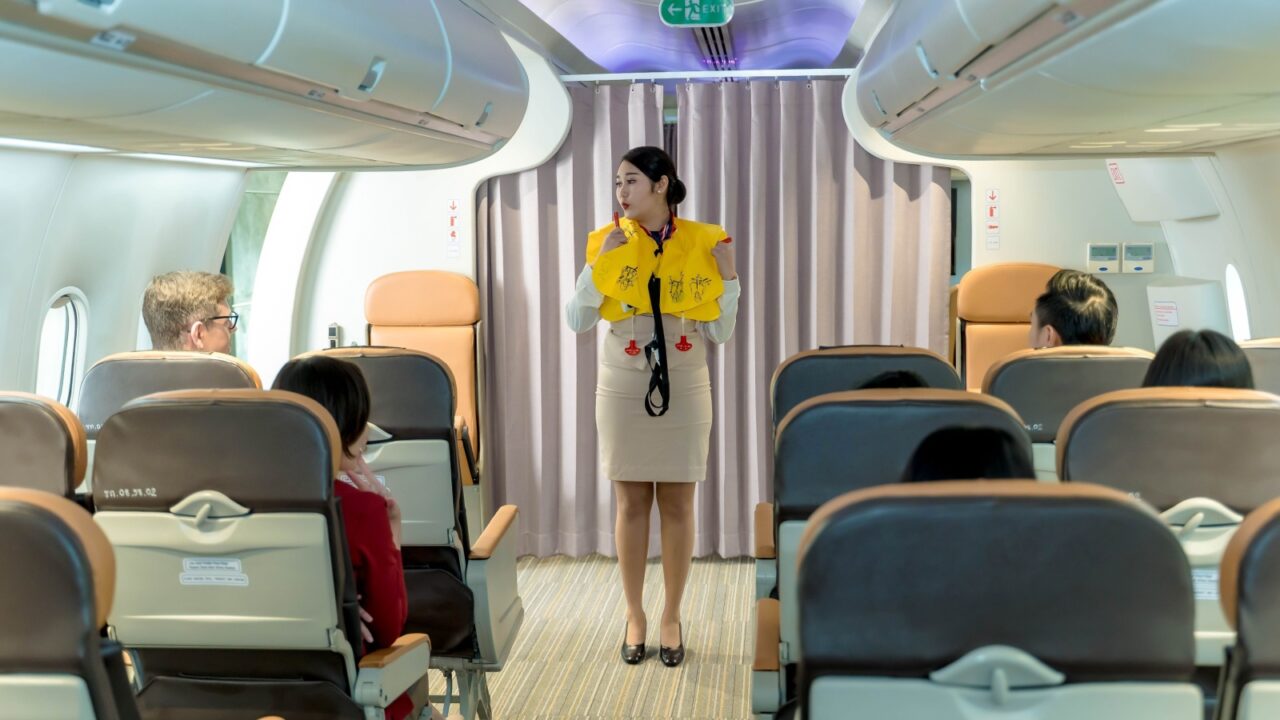 Flight attendant demonstrating life vest inflation to passengers during in-flight safety briefing on a commercial airplane for emergency preparedness awareness