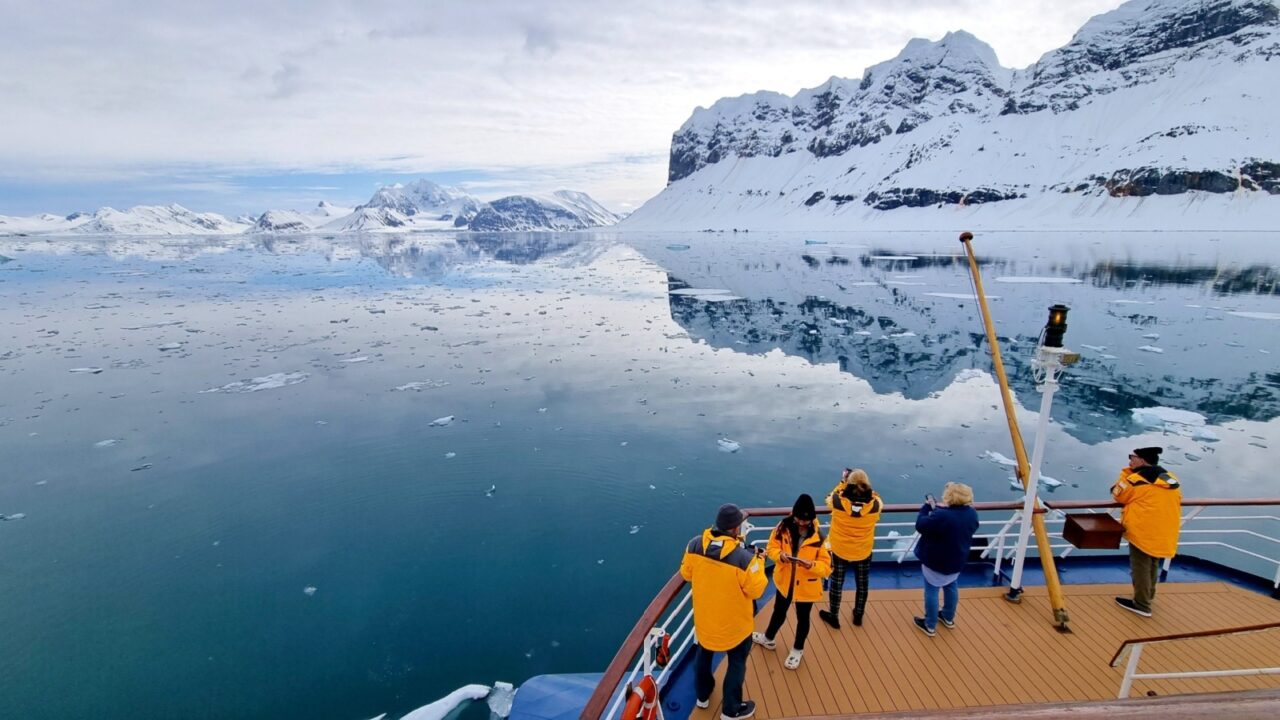 Svalbard, Norway - June 3, 2023: A group of unknown tourists in bright orange jackets admire reflections of the amazing arctic nature from the stern of the expedition ship