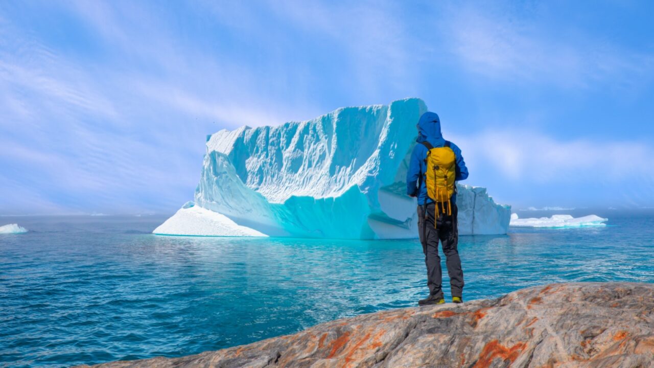 Environmental Concept - A Man Hiker looking at melting Ginat glacier - Melting of a iceberg and pouring water into the sea - Greenland - Tiniteqilaaq, Sermilik Fjord, East Greenland