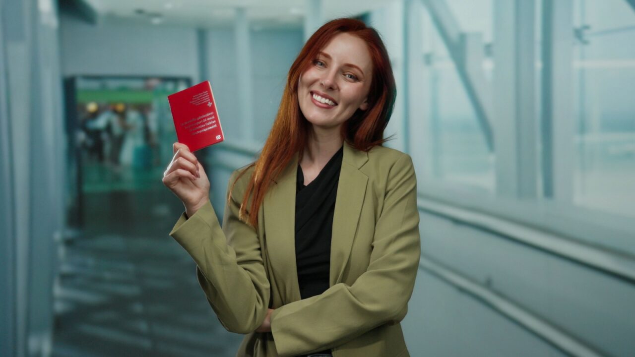 Woman holding swiss passport in airport terminal with a smile, standing in professional attire, emphasizing travel and identity verification.