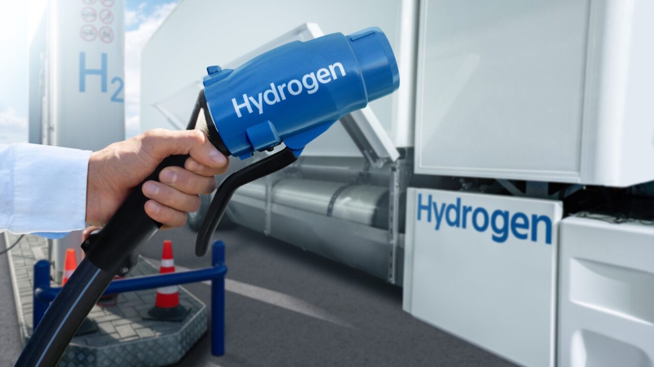 Hand with H2 nozzle on a background of hydrogen fuel cell semi truck with H2 gas cylinder onboard. Eco-friendly commercial vehicle concept.