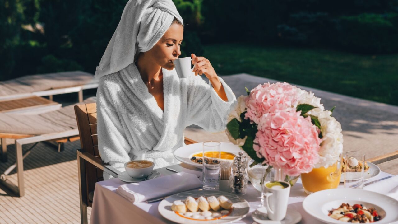 Woman in bathrobe drinking coffee outdoors. breakfast on the summer terrace at the hotel