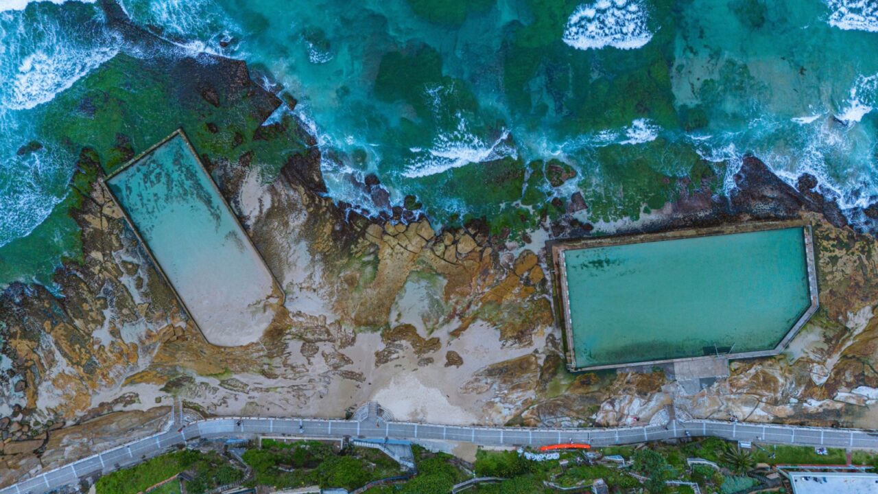 Top-down aerial view from a drone of two pools in the sea that are filled with seawater in Australia.