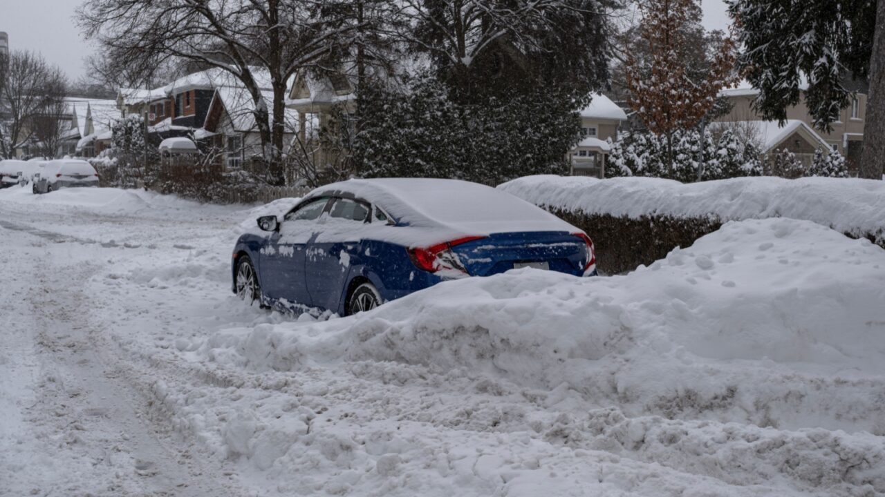 Car covered with snow and stuck on the side of the road due to large snow accumulation and heavy storm in Toronto, Ontario, Canada. Severe weather and unsafe driving condition concept..