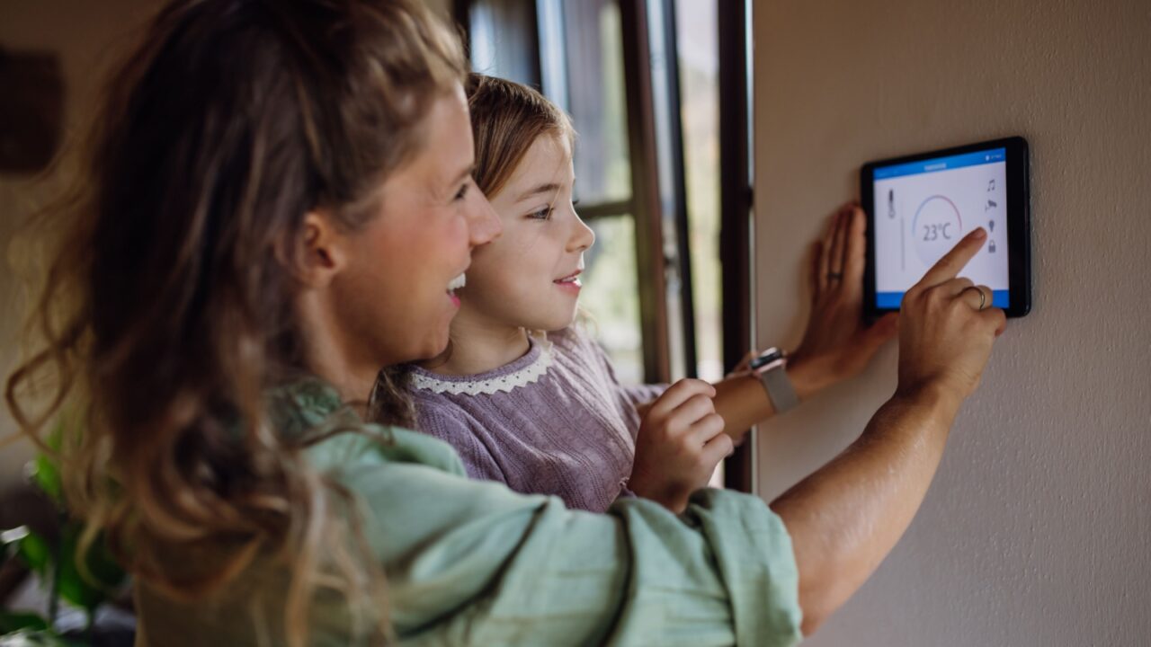 Girl helping mother to adjust, lower heating temperature on thermostat. Concept of sustainable, efficient, and smart technology in home heating and thermostats.