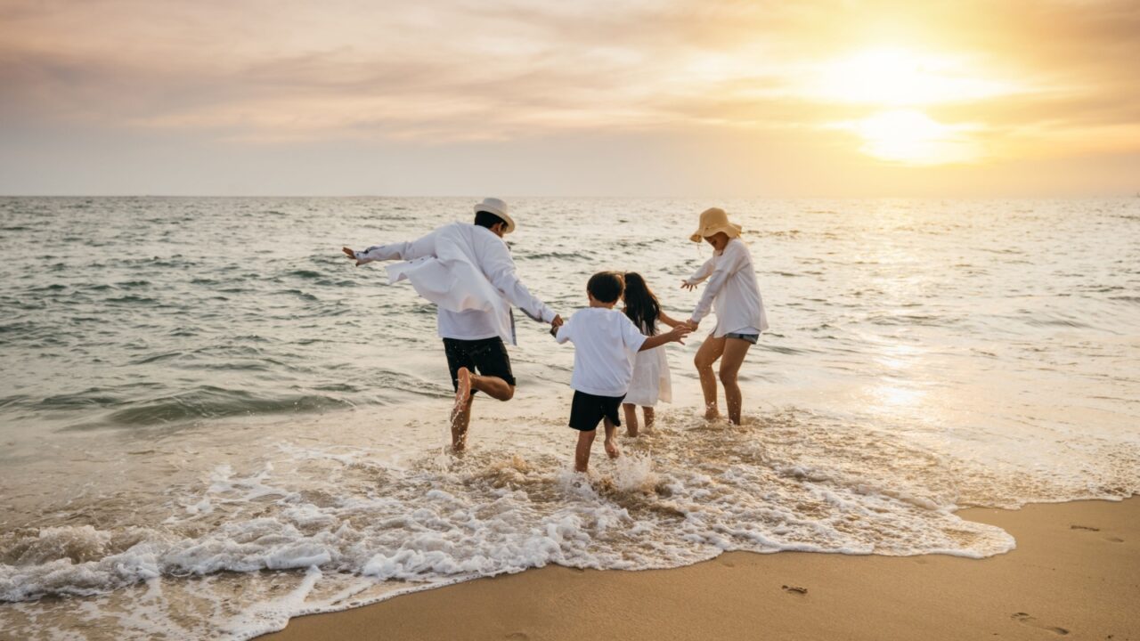 Happy Asian parents and daughters have delightful time on beach. Little girls bond with their mother and father running jumping and pretending to fly with arms wide open. Family fun under sun.