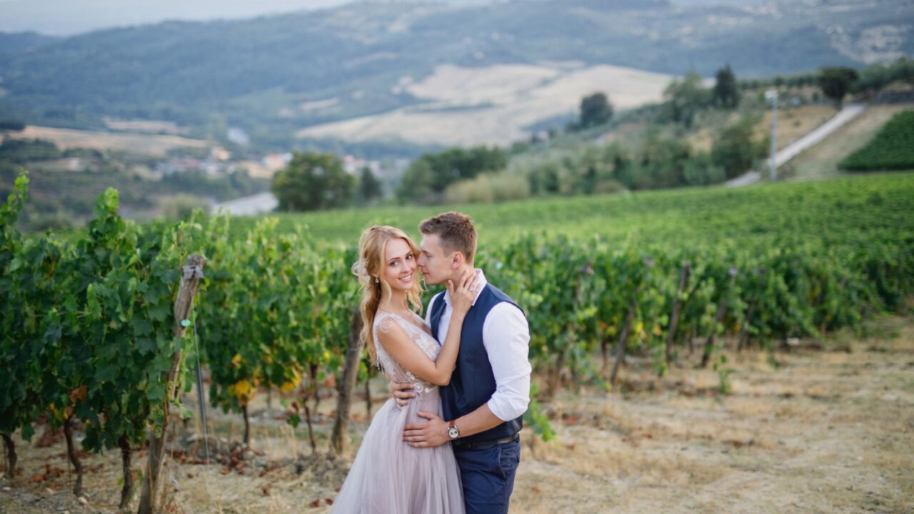 young beautiful wedding couple walking at sunset in Tuscany in Italy near the vineyards bride in beautiful dress groom stylishly dressed