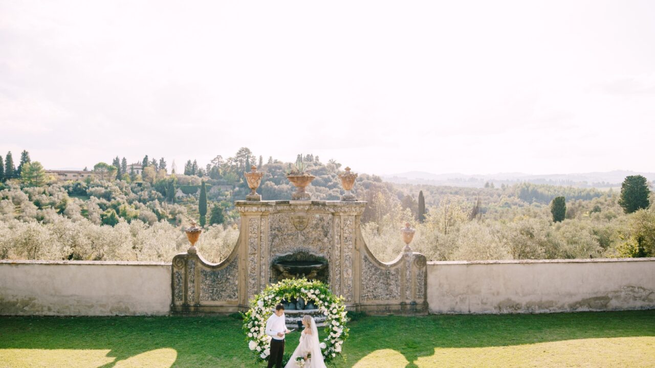 Florence, Italy - 02 october 2019: Wedding at an old winery villa in Tuscany, Italy. Wedding couple under a round arch of flowers. The groom reads wedding vows.