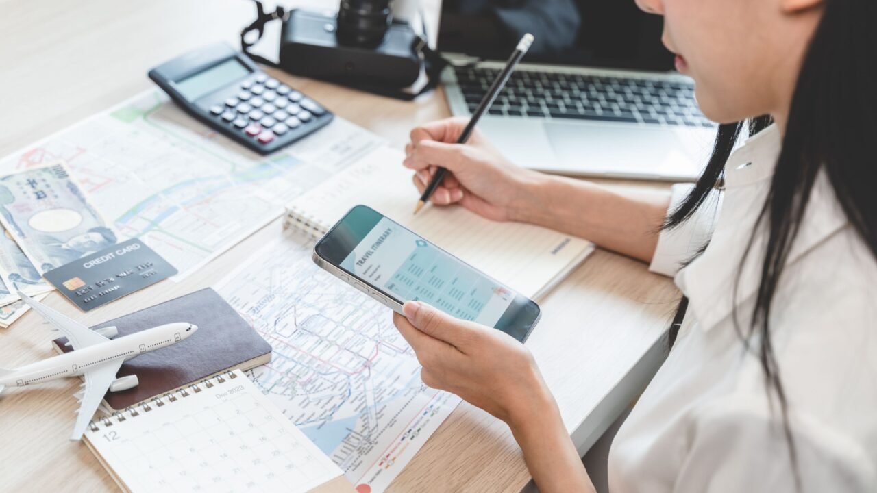 person planning vacation trip to overseas checking tourist destination guide on the map, prepare pocket money, check local transport, booking flight and hotel from mobile application.