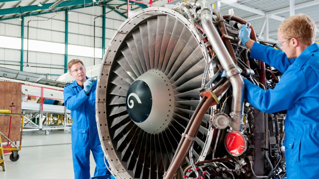 Medium shot of engineers inspecting the turbine engine of a passenger jet at a hangar.