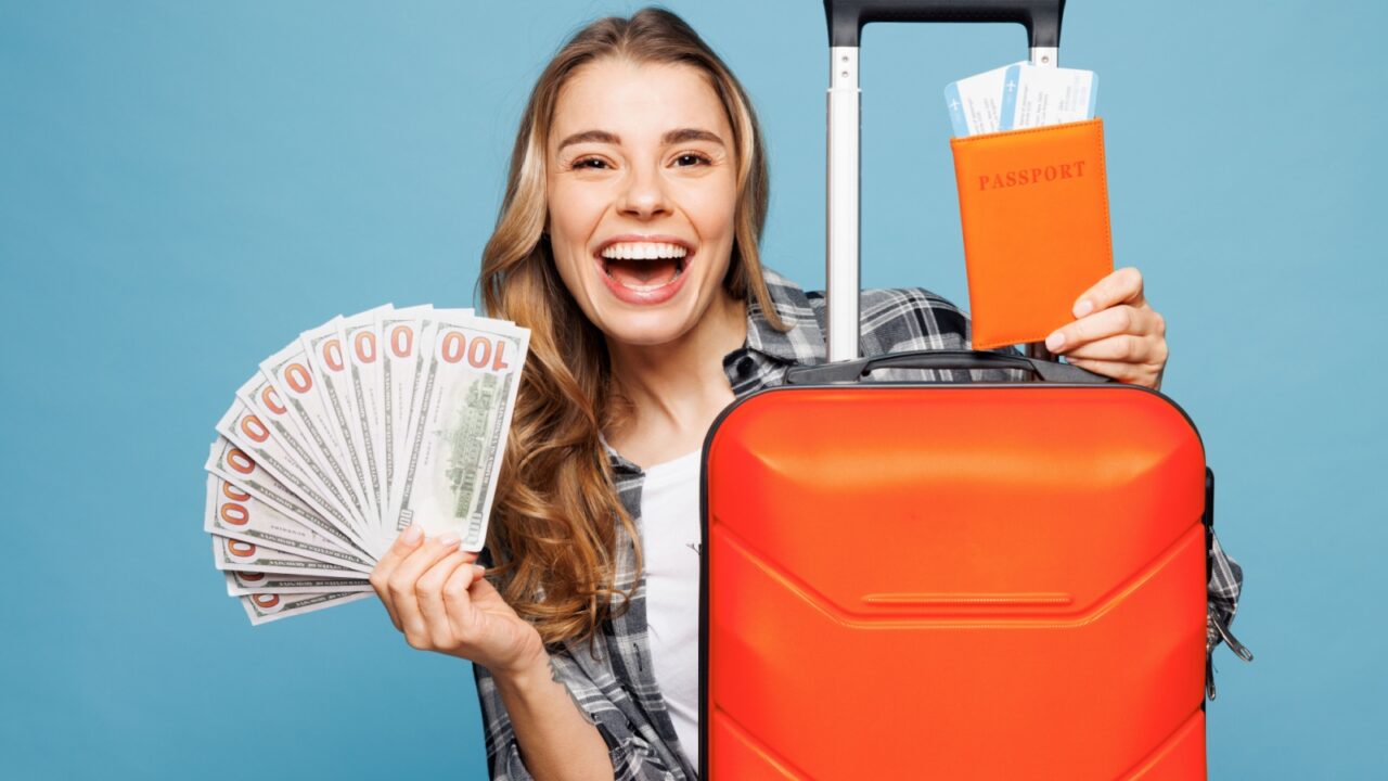 Traveler woman wear grey casual clothes hold passport ticket bag fan of cash money i isolated on plain blue background. Tourist travel abroad in free time rest getaway. Air flight trip journey concept