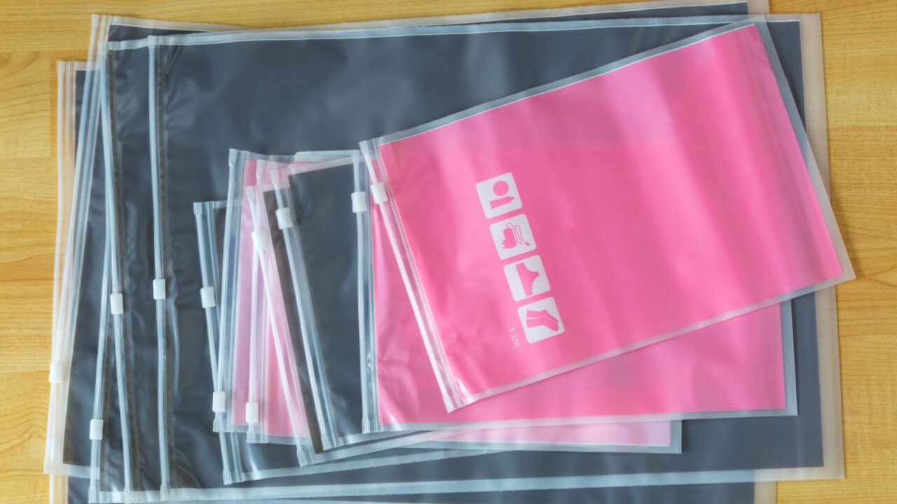 Matte plastic zipper, re-sealable travel bags to store socks, underwear, electronic gadgets, cosmetics, etc top view on wooden background