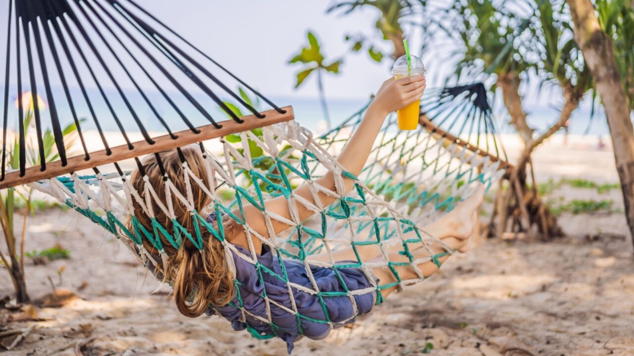 Young woman on the beach in a hammock with a drink